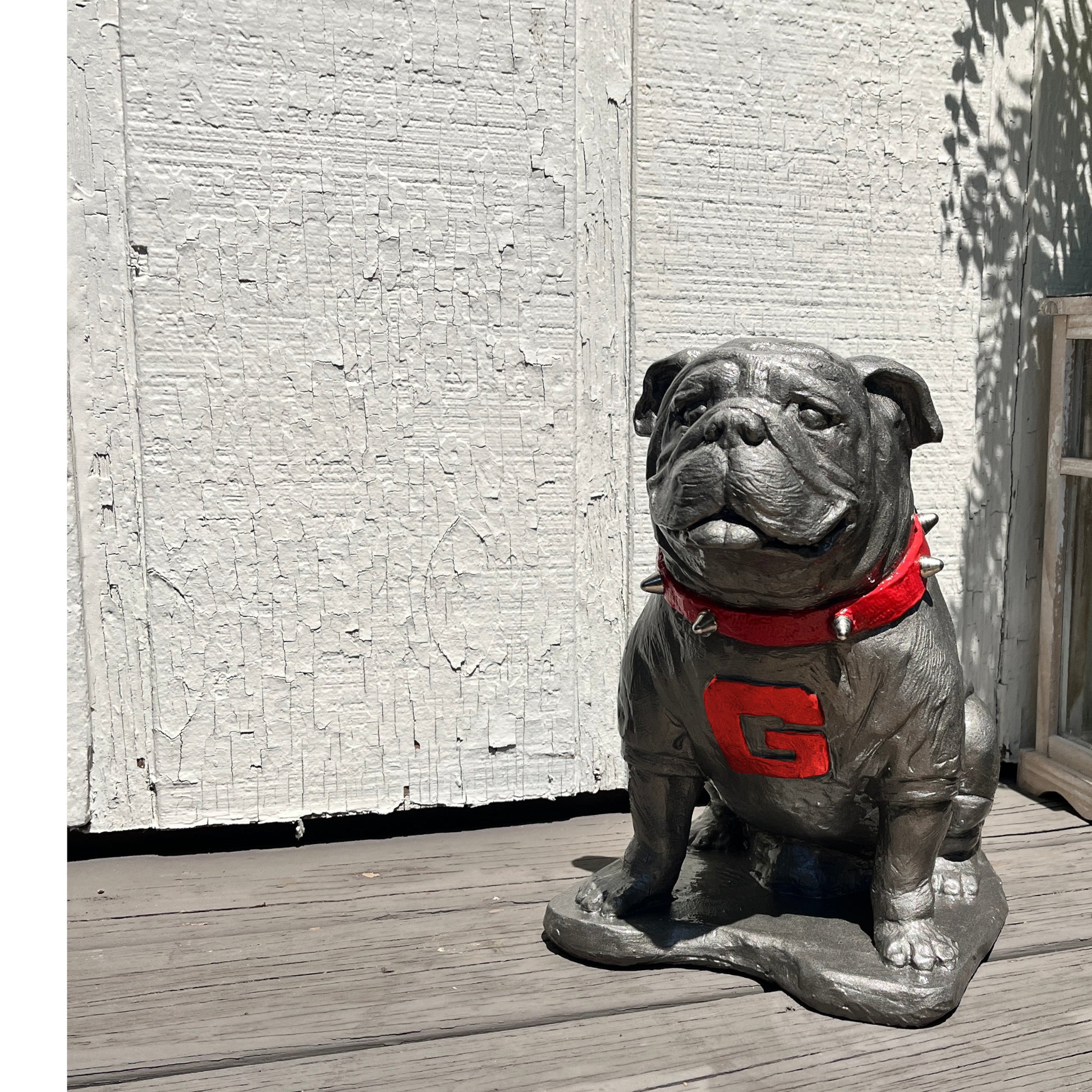 Statue of a bulldog wearing a red sweater with a large 'G' on a wooden deck.